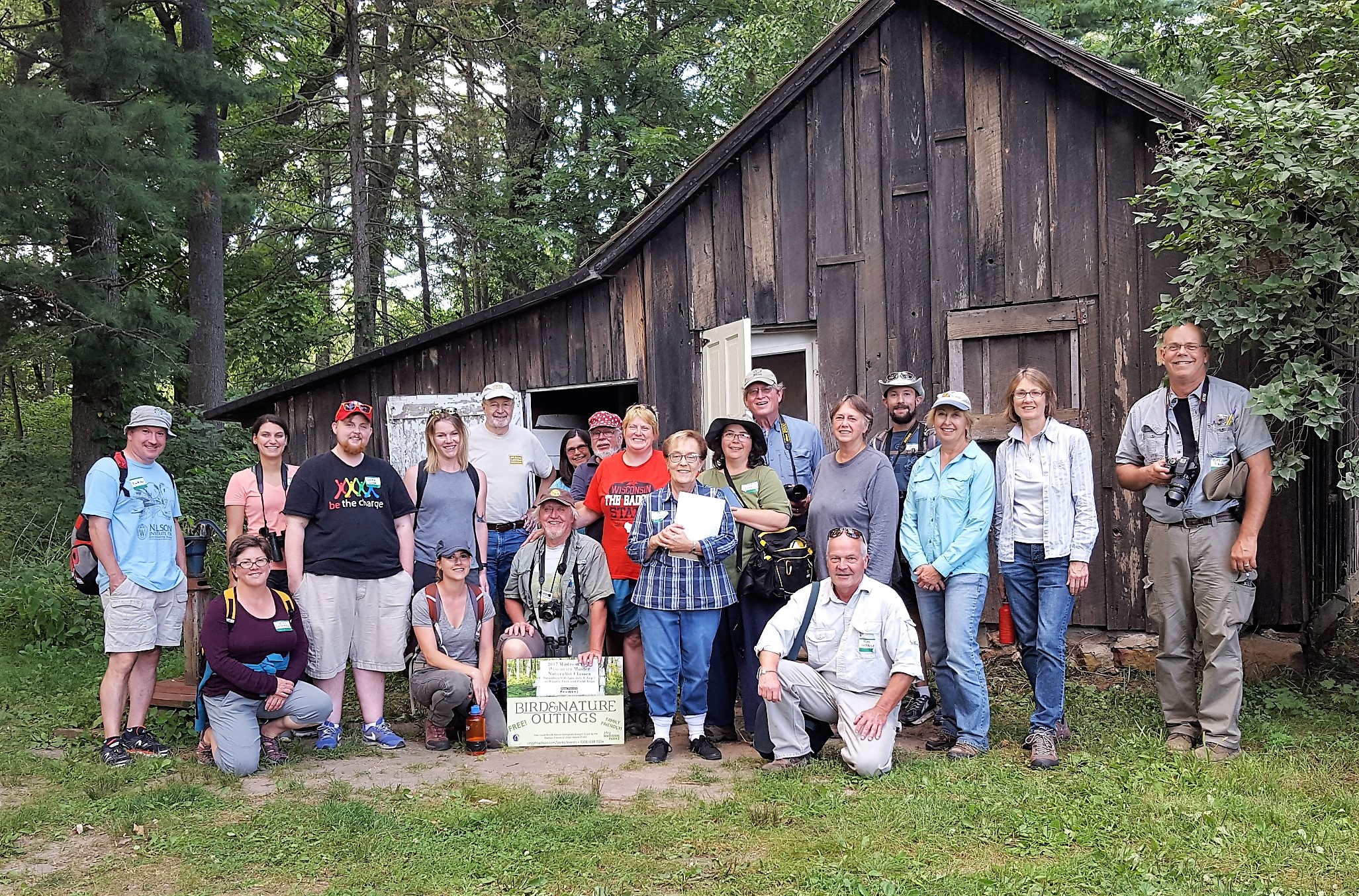 A large group of people standing in front of an old weathered barn