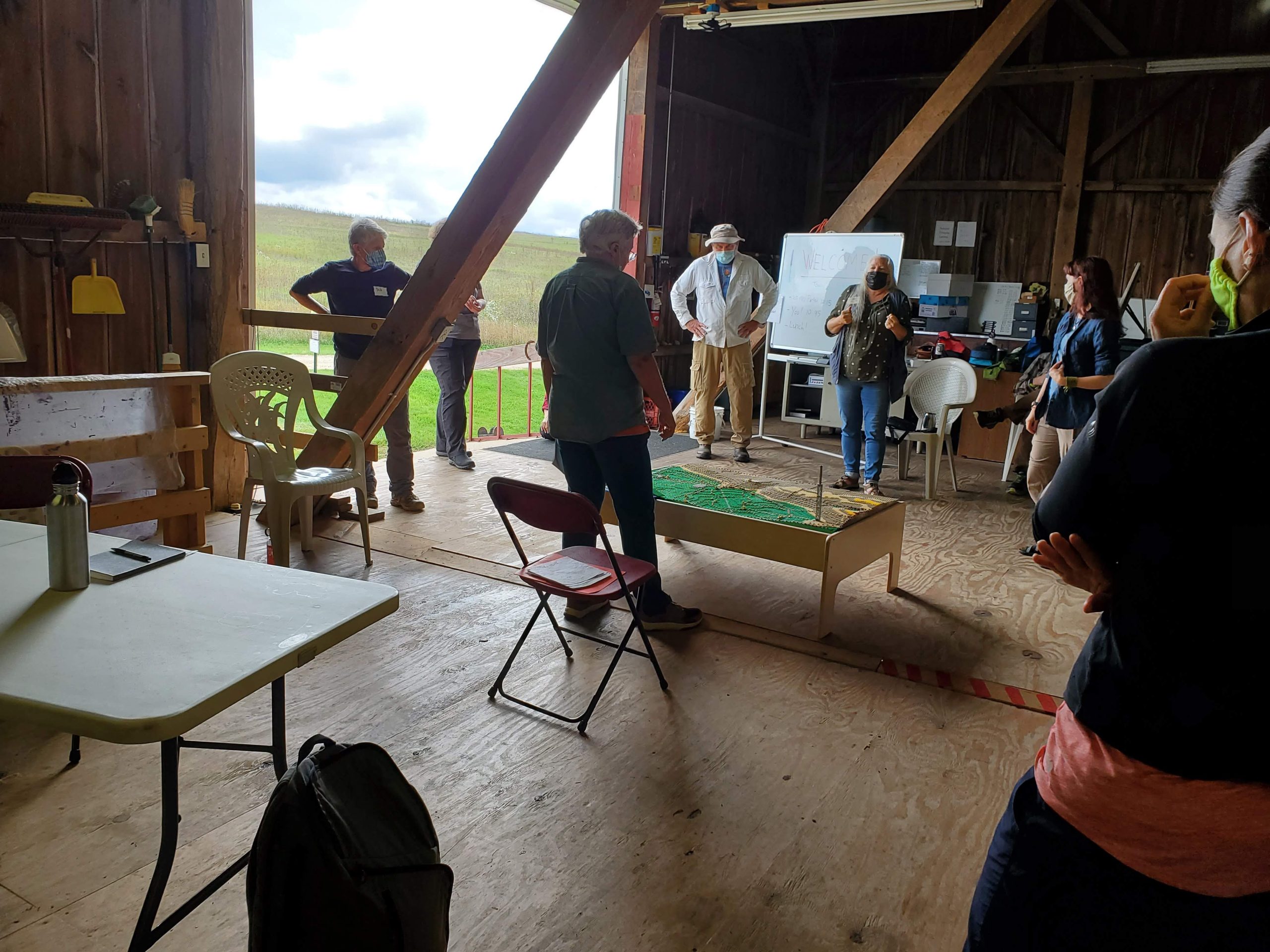 People stand in a barn, looking at and discussing a educational project in teh center of the floor.