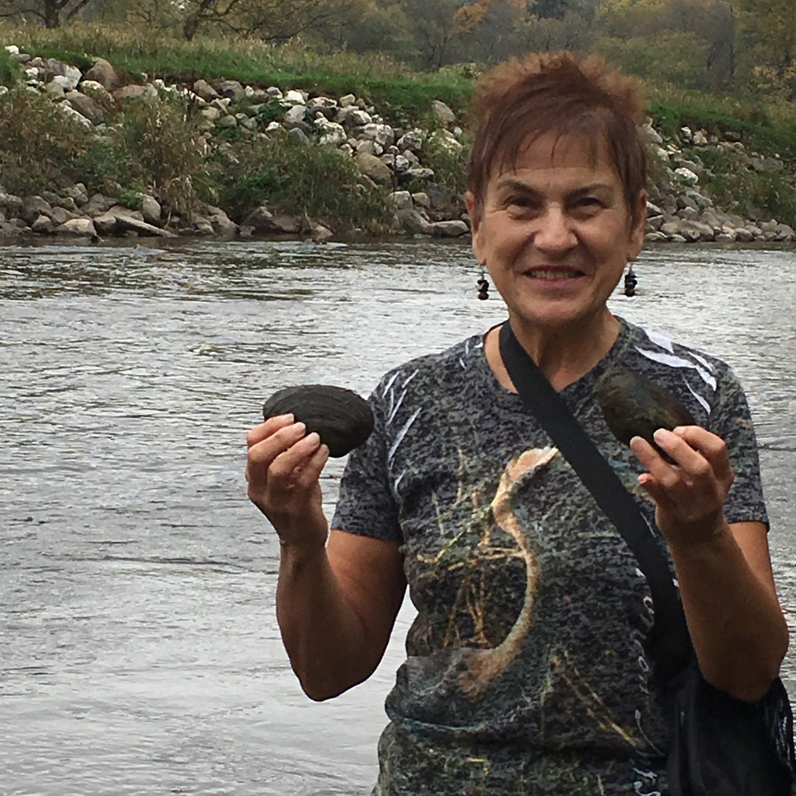 a woman stands along a river holding a musel in each hand