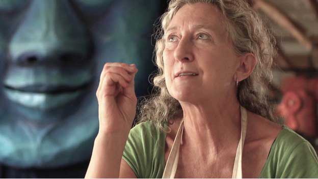 A women sits in an art studio and looks off into the distance.