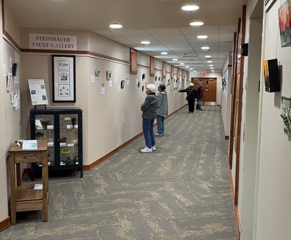 People stand in a long hallway looking at tiny art